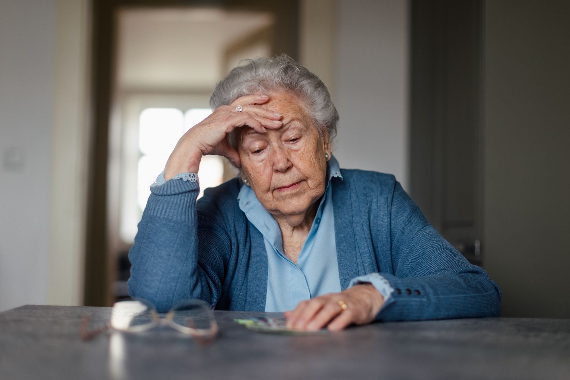 Older woman counts cash on tabletop, stressed
